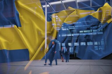 business people walking outside an office building with the national flag of Sweden in the background