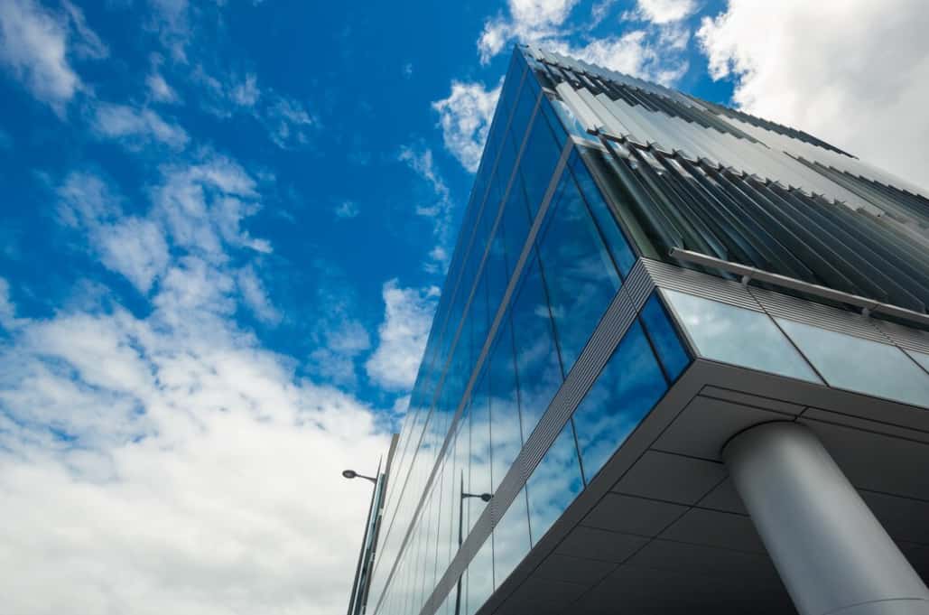 A modern glass skyscraper reaching into a cloudy blue sky